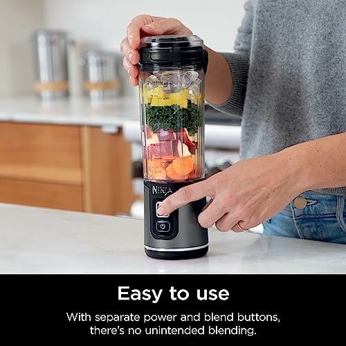 Person using Ninja personal blender with vegetables inside.