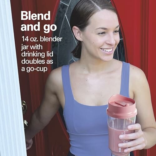 Person holding a 14 oz blender jar with drinking lid, standing by a red door.